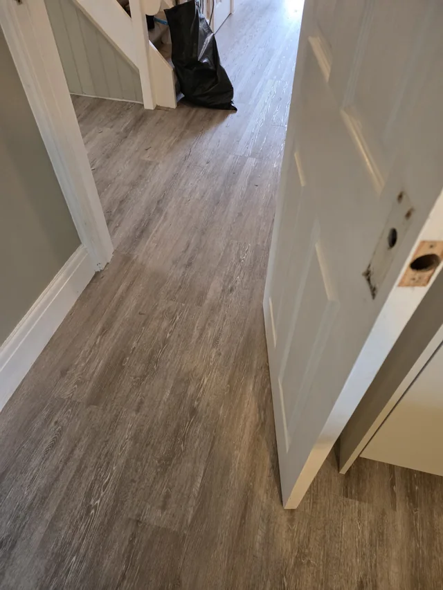 View through an open white door showing the wood-effect LVT planks continuing along the hallway