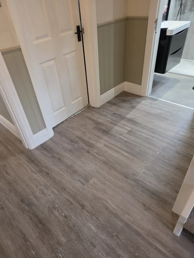 Straight-laid wood-effect LVT across the hallway beside white doors and an adjoining shower-room doorway