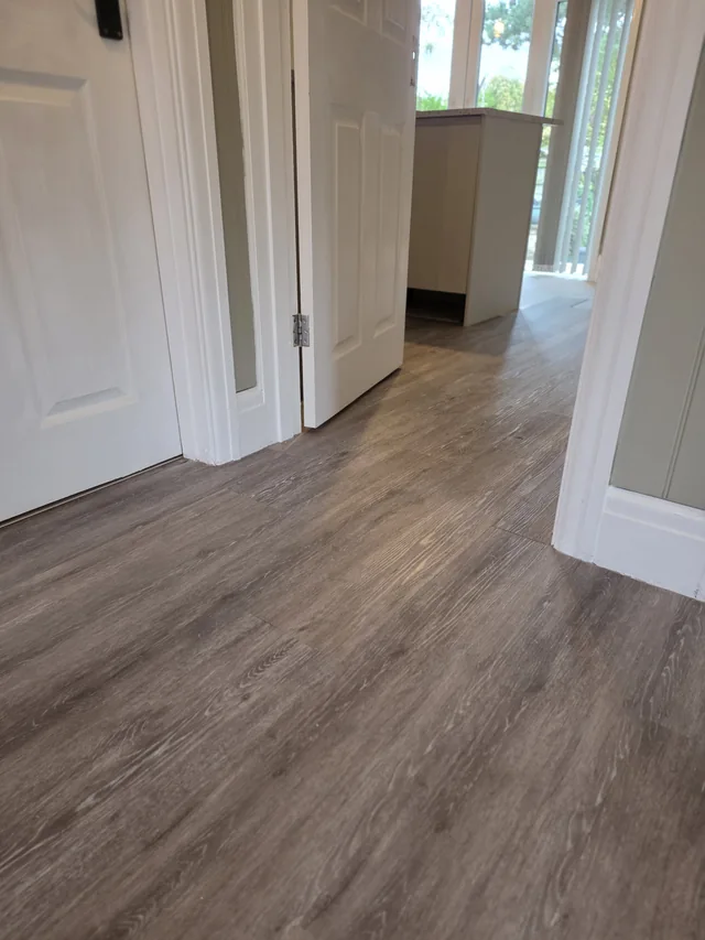 Low view across straight-laid wood-effect LVT planks through an open doorway towards the kitchen