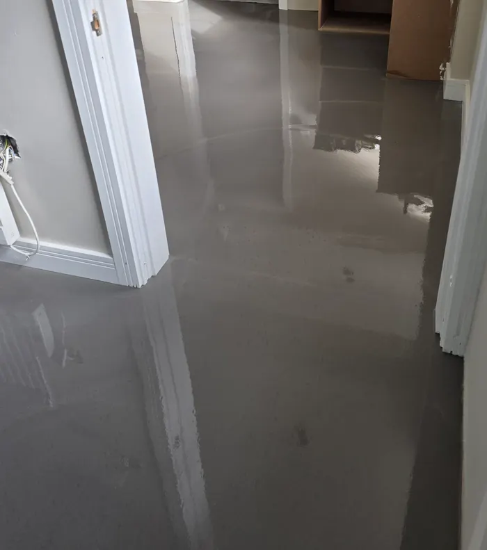 Freshly poured wet smoothing compound running through a hallway and into the next room before flooring is fitted