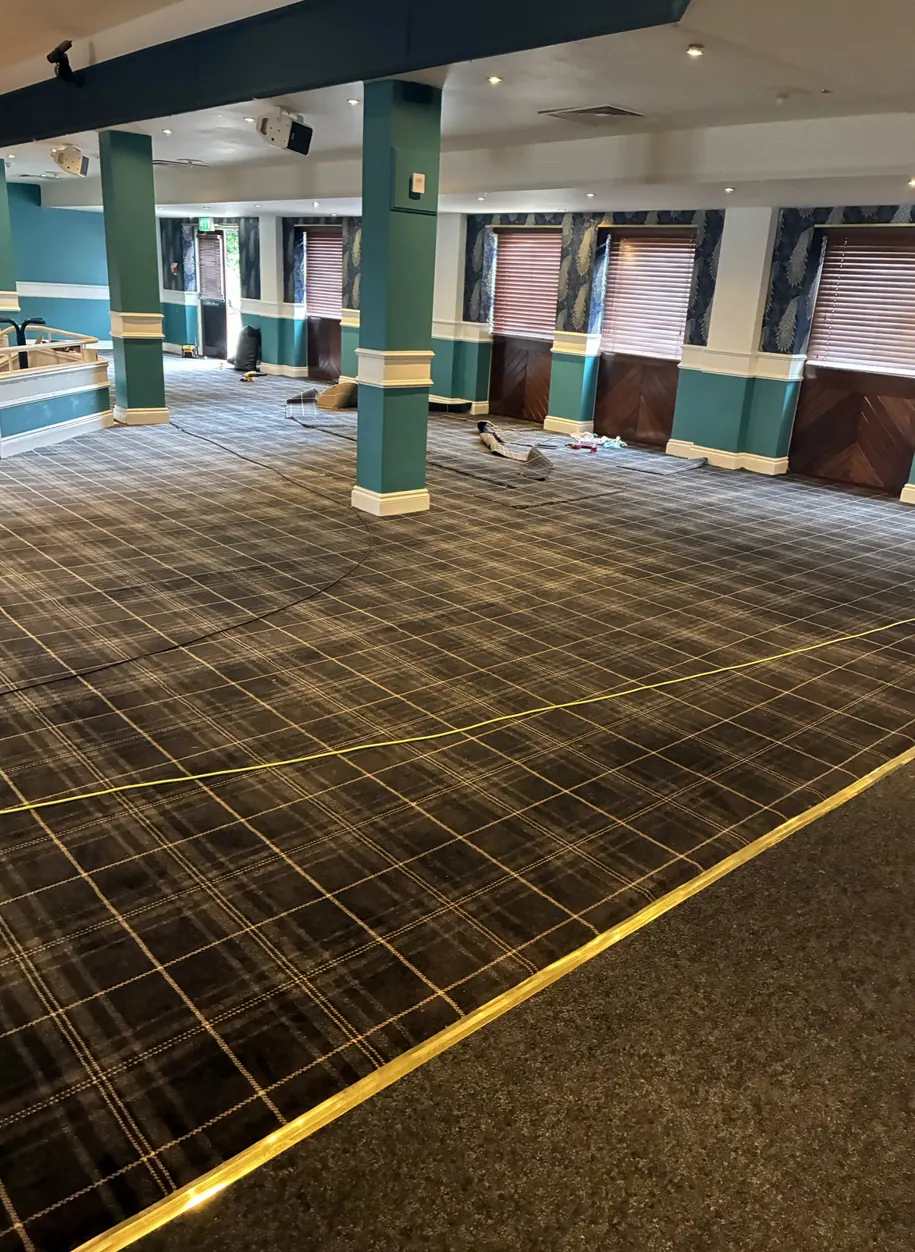 Full room view of the ongoing flooring project at Far Grange Holiday Park, with checked flooring, green columns, windows and a contrasting perimeter strip