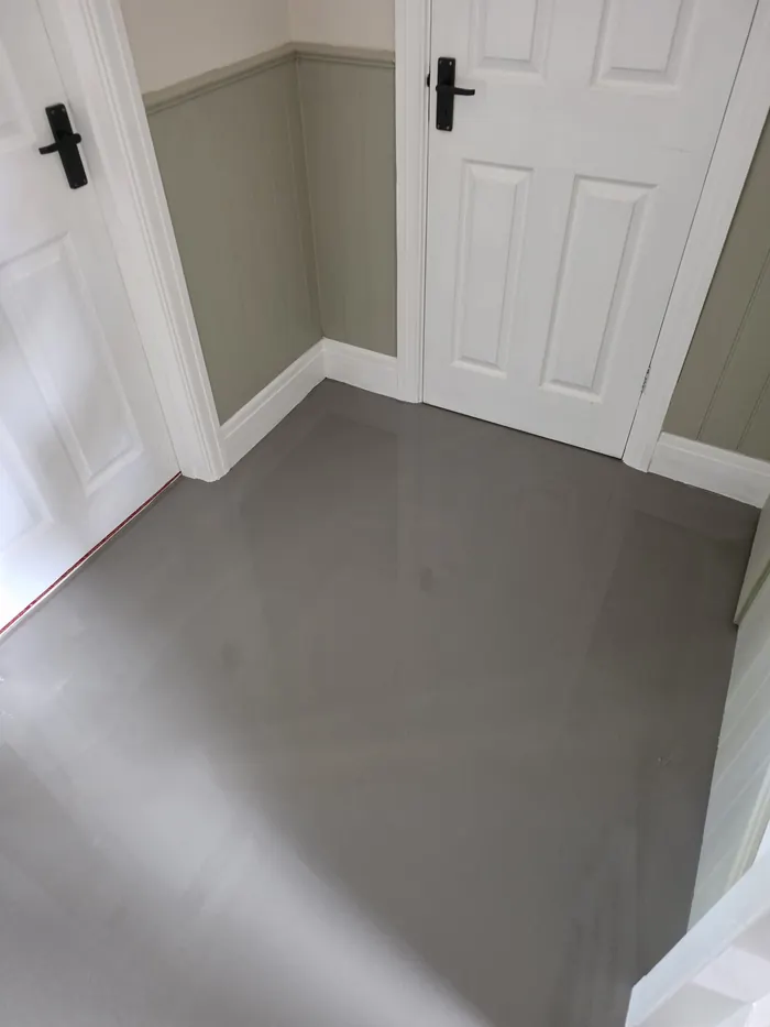 Fresh smooth grey levelling compound before LVT fitting in an entrance hall with white doors and green wall panelling