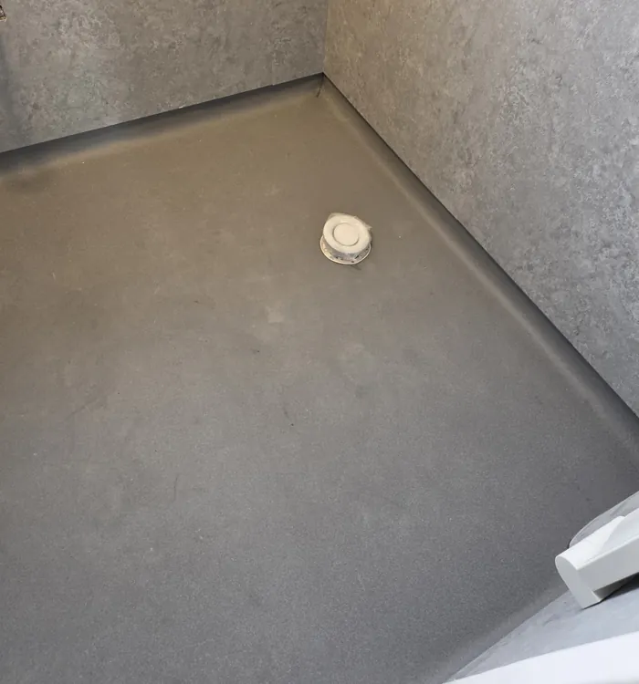 Grey Altro Aquarius wet-room floor with coved edges and a central drain cover, viewed towards a wall-panelled corner